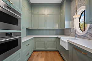 Kitchen featuring double oven, green cabinets, light wood finished floors, light stone counters, and decorative backsplash