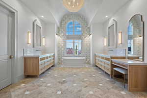 Full bathroom with lofted ceiling, a freestanding tub, two vanities, recessed lighting, and a chandelier