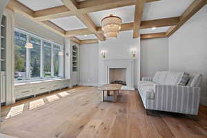 Sitting room with beamed ceiling, light wood finished floors, coffered ceiling, and a chandelier