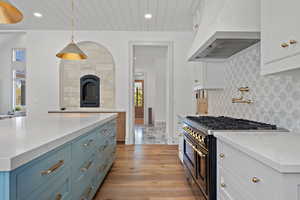 Kitchen with light stone countertops, high end black range oven, custom exhaust hood, pendant lighting, and white cabinetry