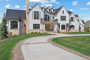 View of front of home featuring a front lawn, a balcony, board and batten siding, stone siding, and roof with shingles
