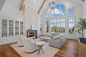 Living area featuring a stone fireplace, wood finished floors, beam ceiling, high vaulted ceiling, and plenty of natural light
