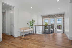 Hall featuring an upstairs landing, light wood-type flooring, brick wall, and recessed lighting