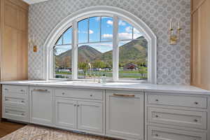 Kitchen featuring a mountain view, light stone counters, wallpapered walls, and white cabinets