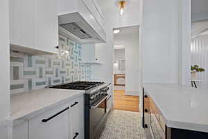 Kitchen with gas range, tasteful backsplash, custom exhaust hood, white cabinetry, and light stone countertops