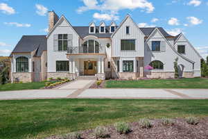 View of front facade with a balcony, a front yard, a chimney, board and batten siding, and stone siding