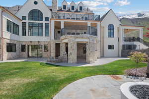 Back of house with a balcony, a patio area, a yard, a mountain view, and stairs