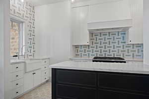 Kitchen with dark cabinets, white cabinets, light stone countertops, tasteful backsplash, and exhaust hood