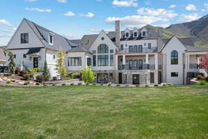 Rear view of property featuring a balcony, a yard, a shingled roof, a chimney, and stone siding
