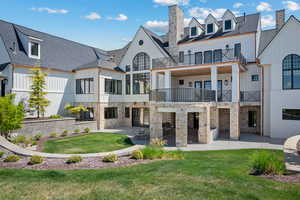 Rear view of house with a balcony, a patio area, board and batten siding, and a lawn
