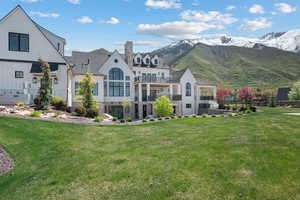Back of house featuring stone siding, a balcony, a chimney, a lawn, and a mountain view