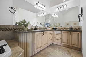Primary bath featuring double vanity, decorative backsplash, crown molding, light tile patterned flooring, and a bathtub