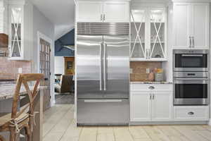 Kitchen featuring glass insert cabinets, decorative brick backsplash, stainless steel appliances, and white cabinetry