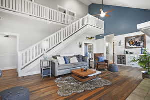 Living room with high vaulted ceiling, ceiling fan, wood-style floors, fireplace and stairway