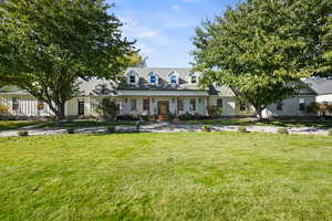Cape cod/Rambler style home featuring a covered porch, a large front yard with circular driveway, and board and batten siding