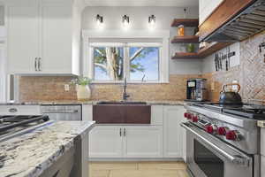Kitchen featuring appliances with stainless steel finishes, light stone countertops, exhaust hood, white cabinets, and open shelves