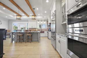 Kitchen featuring premium appliances, white cabinetry, a kitchen bar, hanging light fixtures, and light stone counters