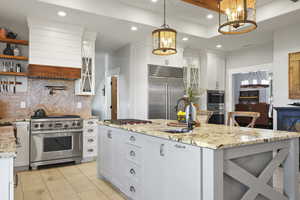 Kitchen featuring white cabinets, glass insert cabinets, high end appliances, light stone countertops, and recessed lighting