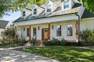 Cape cod/Rambler style home featuring a covered porch, a large front yard with circular driveway, and board and batten siding