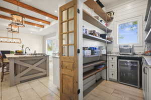 Kitchen featuring light stone countertops, beverage cooler, hanging light fixtures, white cabinetry, and beamed ceiling
