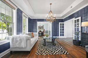 Living room featuring dark wood-type flooring, a tray ceiling, French doors, a chandelier, and crown molding