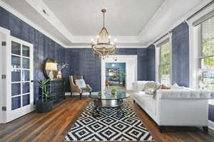 Living area featuring a raised ceiling, dark wood-style floors, a chandelier, ornamental molding, and French doors