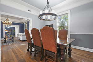Dining area with a chandelier, dark wood-style floors, a tray ceiling, and ornamental molding