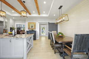Kitchen featuring a barn door, pendant lighting, white cabinetry, light stone counters, and a chandelier
