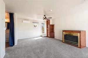 Unfurnished living room featuring a glass covered fireplace, carpet flooring, ceiling fan, and a wall mounted air conditioner