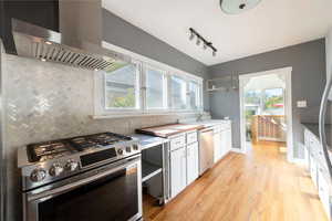 Kitchen featuring appliances with stainless steel finishes, wall chimney range hood, decorative backsplash, and white cabinets