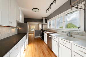 Kitchen featuring white cabinets, decorative backsplash, stainless steel appliances, wall chimney exhaust hood, and light wood-style floors