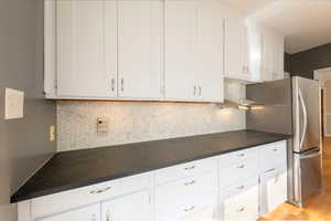 Kitchen with tasteful backsplash, white cabinetry, freestanding refrigerator, dark countertops, and light wood-style flooring