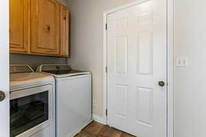 Laundry area with dark tile patterned flooring, cabinet space, and washing machine and clothes dryer