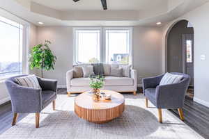 Living area featuring wood finished floors, arched walkways, ceiling fan, a tray ceiling, and recessed lighting