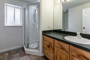 Bathroom featuring vanity, a shower stall, a chandelier, and dark tile patterned flooring