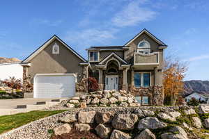 View of front of property with stone siding, driveway, stucco siding, a mountain view, and an attached garage