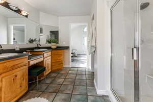 Bathroom featuring double vanity, a shower stall, and dark tile patterned floors