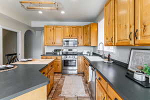 Kitchen featuring dark countertops, appliances with stainless steel finishes, light tile patterned flooring, recessed lighting, and arched walkways