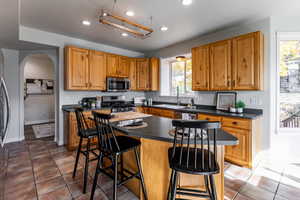 Kitchen featuring dark countertops, light tile patterned floors, recessed lighting, a breakfast bar area, and arched walkways
