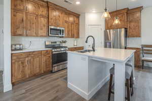 Kitchen featuring brown cabinetry, hanging light fixtures, backsplash, stainless steel appliances, and recessed lighting