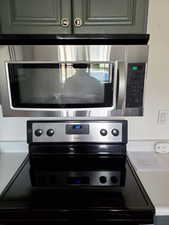 Kitchen view of stainless steel microwave, electric stove, light countertops, and gray cabinetry