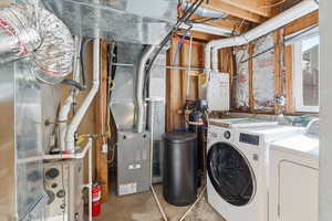 Laundry area with concrete flooring, heating unit, washer and clothes dryer, and water heater
