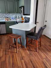 Kitchen featuring a breakfast bar area, stainless steel appliances, light countertops, dark wood finished floors, and backsplash