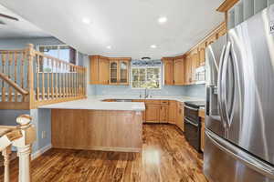 Kitchen featuring appliances with stainless steel finishes, a peninsula, glass insert cabinets, recessed lighting, and dark wood-style flooring