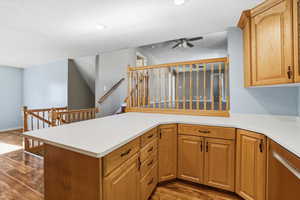 Kitchen with dark wood-type flooring, brown cabinets, a peninsula, ceiling fan, and a textured ceiling