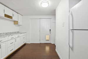 Kitchen with freestanding refrigerator, white cabinets, a textured ceiling, and dark wood finished floors
