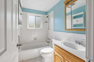 Bathroom with bathing tub / shower combination, vanity, wainscoting, and light tile patterned floors