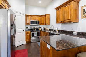 Kitchen featuring appliances with stainless steel finishes, a peninsula, brown cabinets, and dark stone counters