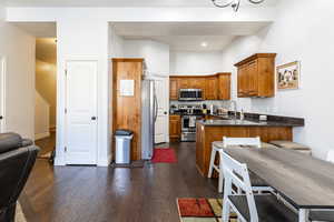 Kitchen with dark wood-style floors, brown cabinetry, a peninsula, appliances with stainless steel finishes, and dark stone countertops