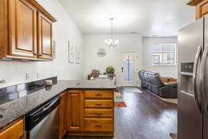 Kitchen with a peninsula, stainless steel appliances, dark stone counters, brown cabinets, and dark wood-style floors